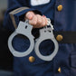 A person in a dark blue uniform holds plastic toy handcuffs from the Great Pretenders Police Officer Set, ready for dress-up or role-playing.