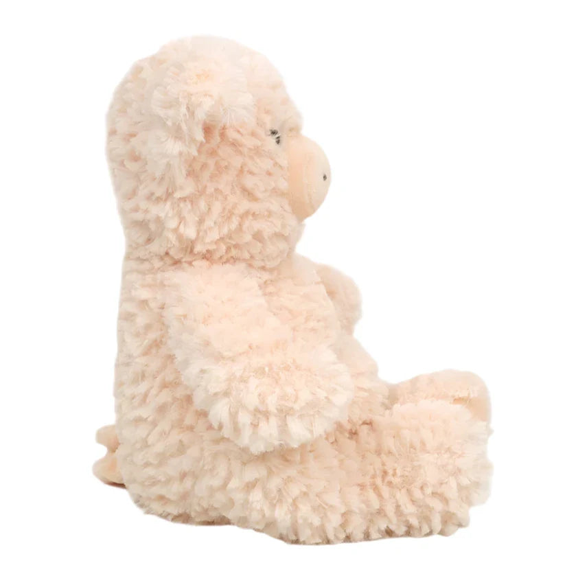 A side view of Mon Ami's Polly Pig, a light pink, fluffy stuffed animal resembling a bear, shown sitting upright against a white background.