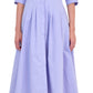Someone wearing the Simkhai Signature Jazz Dress, a light blue cotton poplin, long-sleeve, collared midi with an A-line pleated skirt, paired with white sandals.