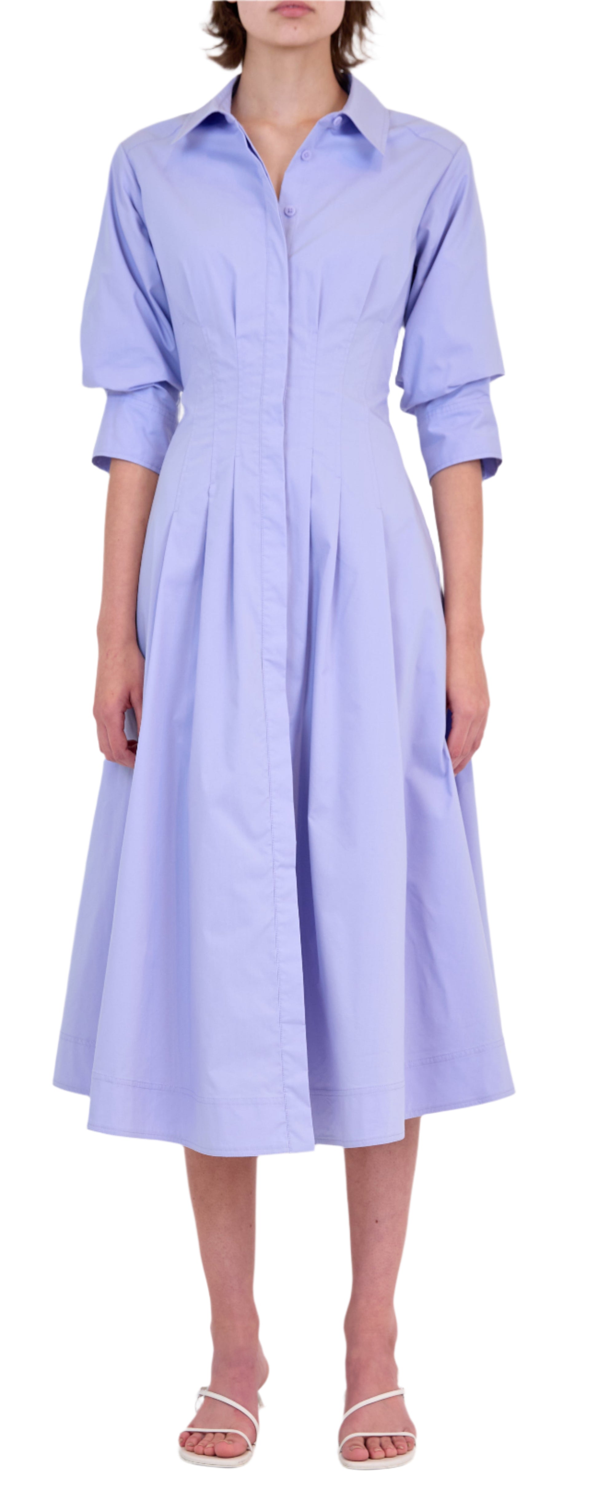 Someone wearing the Simkhai Signature Jazz Dress, a light blue cotton poplin, long-sleeve, collared midi with an A-line pleated skirt, paired with white sandals.