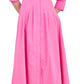 A woman wears the Signature Jazz Dress by Simkhai, a long-sleeved pink cotton poplin midi with pintucks, pockets, and an A-line silhouette, paired with white heeled sandals.