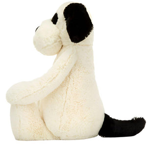 Side view of a seated Jellycat Bashful Black & Cream Puppy, Really Big, featuring silky-soft cream fur with black ears and tail.