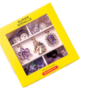 A yellow box labeled "Super Smalls Make It Purple Mini Bead Kit" contains a collection of beads and charms focused on a purple theme, featuring unique items such as unicorn and flower charms, ideal for crafting one-of-a-kind jewelry.