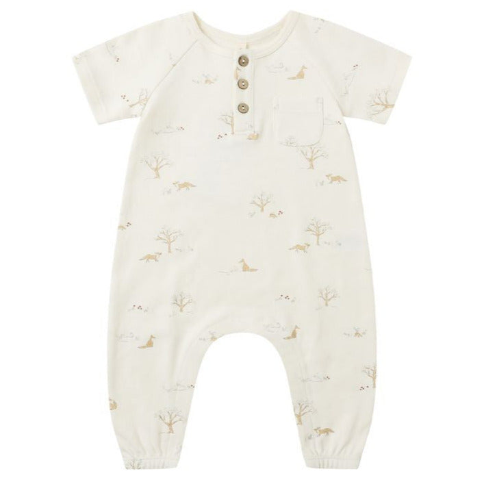 The Quincy Mae Baby Short Sleeve Jumpsuit features a cream color, three coconut buttons, a chest pocket, and a subtle animal and tree print—designed for babies with easy changing in mind.