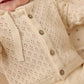 A baby in a cream Quincy Mae Baby Girls' and Girls' Knit Cardigan with coconut buttons and a matching outfit, lying on a patterned blanket.