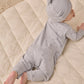 A baby wears the Quincy Mae Baby Boys’ Long Sleeve Jumpsuit in light gray, featuring coconut buttons and inseam snaps, while lying on their stomach on a cream-colored quilted blanket.