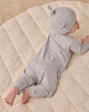 A baby wears the Quincy Mae Baby Boys’ Long Sleeve Jumpsuit in light gray, featuring coconut buttons and inseam snaps, while lying on their stomach on a cream-colored quilted blanket.