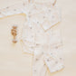 Flat lay of the Quincy Mae Baby Side Snap Bodysuit + Pant Set, featuring a white bodysuit and matching footed pants with small animal prints, displayed beside a wooden rattle on a light background—perfect for keeping your newborn cozy.