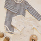 Two baby boys’ ribbed bodysuits from Quincy Mae’s 2-pack set, including one in grey with white stripes and another in cream featuring moons and stars, are displayed on a light surface alongside wooden toys and acorns.