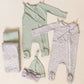 Two sets of baby pajamas, including the Quincy Mae Baby Boys' Bamboo Zip Footie, matching hats, and blankets, are displayed on a neutral background. One is green plaid; the other has a pastel floral print.