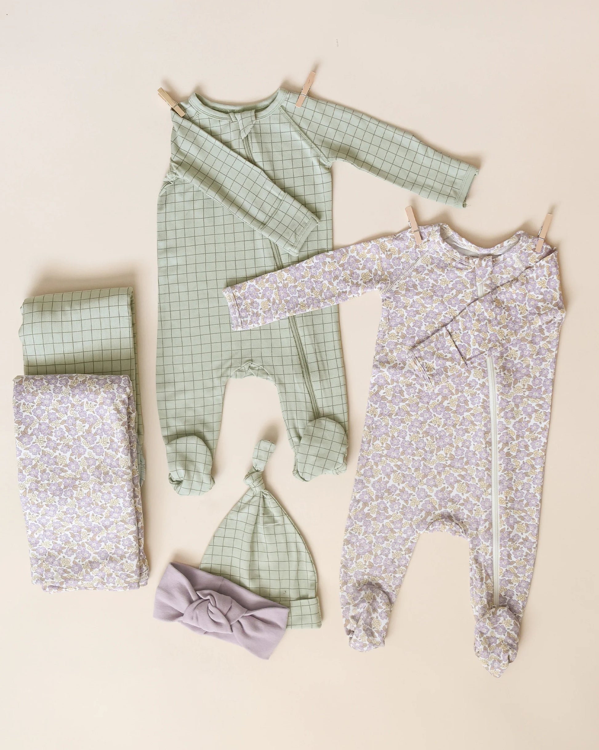 Two sets of baby pajamas, including the Quincy Mae Baby Boys' Bamboo Zip Footie, matching hats, and blankets, are displayed on a neutral background. One is green plaid; the other has a pastel floral print.