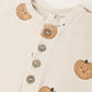 Close-up of the Quincy Mae Baby Relaxed Fleece Jumpsuit in cream, featuring three buttons and a cheerful pattern of smiling orange pumpkins—crafted for everyday comfort as a cozy essential in your little one’s wardrobe.