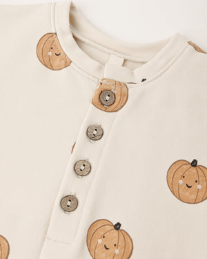 Close-up of the Quincy Mae Baby Relaxed Fleece Jumpsuit in cream, featuring three buttons and a cheerful pattern of smiling orange pumpkins—crafted for everyday comfort as a cozy essential in your little one’s wardrobe.
