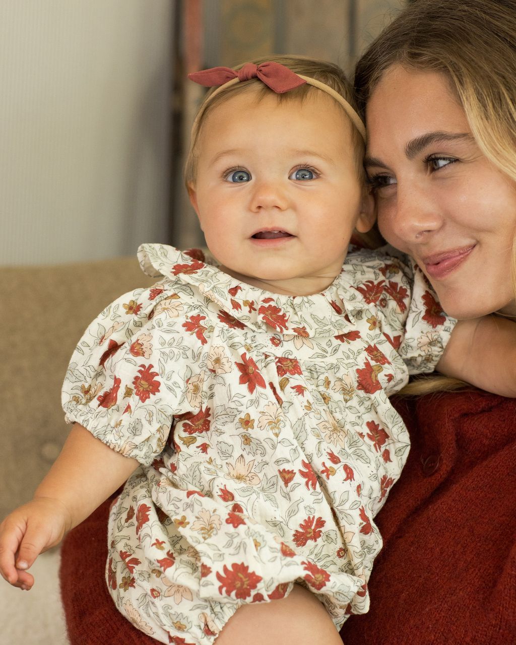 A baby in the Rylee & Cru Baby Girls' Lula Romper sits on a woman's lap, both smiling and looking the same way.