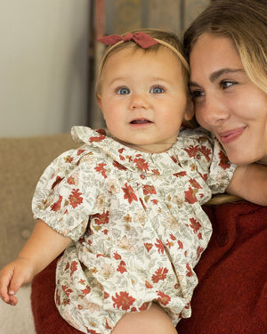 A baby in the Rylee & Cru Baby Girls' Lula Romper sits on a woman's lap, both smiling and looking the same way.