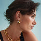 A person with short brown hair wears Lizzie Fortunato's Mixed Metal Bubble Hoops and a chunky gold chain necklace, gazing right against a light blue background.