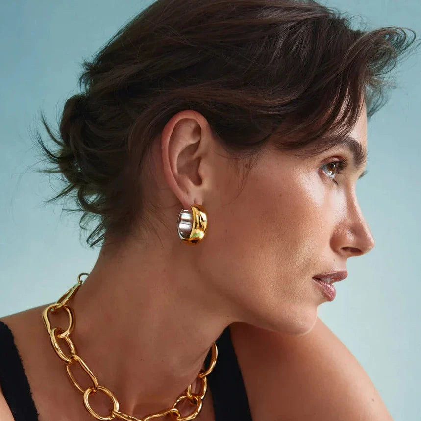 A woman with a serious expression, wearing a chunky gold and silver-plated brass necklace and Lizzie Fortunato Mixed Metal Bubble Hoops.