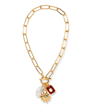 The Helios Charm Necklace by Lizzie Fortunato features a gold chain with large links, accented by a white freshwater pearl, a red rectangular charm, and a gold sunburst charm set with a small green stone.