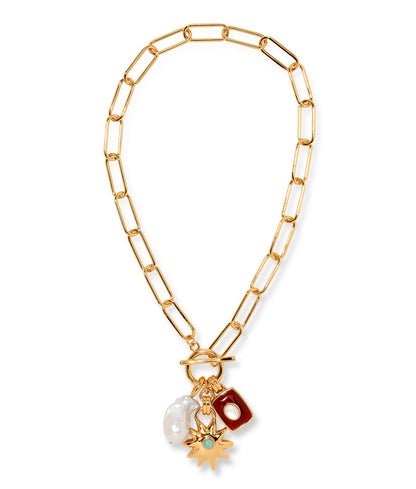 The Helios Charm Necklace by Lizzie Fortunato features a gold chain with large links, accented by a white freshwater pearl, a red rectangular charm, and a gold sunburst charm set with a small green stone.