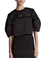 A person dressed in a Lela Rose Iris Top with lantern sleeves and detailed inset lace panels on the neckline, paired with a black skirt.