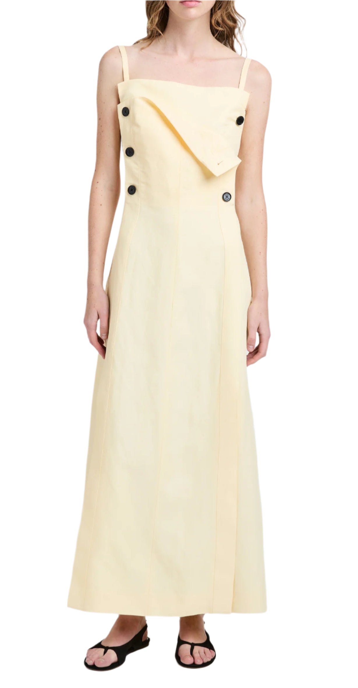 Someone is wearing the Candice Dress by Proenza Schouler, a sailor-inspired beige dress with a long, sleeveless design featuring black buttons and a folded front accent, paired with black sandals.