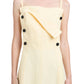 Front view of a person wearing the Candice Dress by Proenza Schouler, featuring a light yellow sailor-inspired design with black buttons and an asymmetrical flap detail.