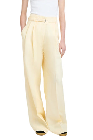 A person exudes style in the chic Jules Pant by Proenza Schouler, featuring a high-waisted, wide-leg silhouette in beige linen viscose. They're cinched at the waist with a white belt and paired elegantly with a crisp white top.