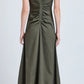 Wearing the Proenza Schouler Remi Dress in olive green eco stretch linen, featuring a sleeveless cut, V-shaped back, and gathered center detail, a person stands against a plain background.