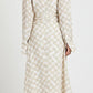 A woman faces away, wearing the Proenza Schouler Keria Printed Crepe De Chine Dress—a beige and white checkered, long-sleeved midi with a gathered twist detail—paired with black flat shoes.