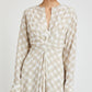 A woman wears the Proenza Schouler Keria Printed Crepe De Chine Dress in beige and white check, featuring gathered twist detail and flared cuffs, standing against a plain background.