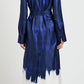 A person wearing the Proenza Schouler Amaya Silk Twill Dress, a long-sleeve blue shirtdress with a white hem and belt, stands with their back to the camera against a plain background.