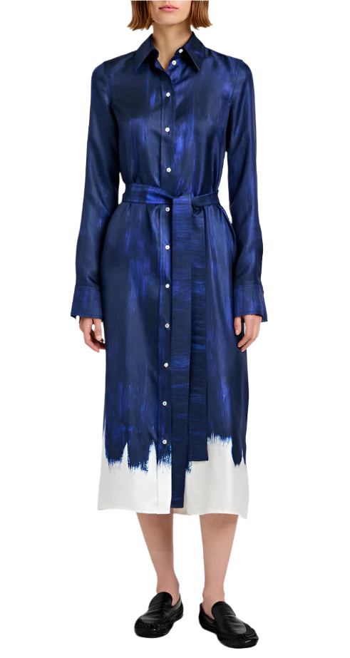 A woman wears the Proenza Schouler Amaya Silk Twill Dress—navy blue, long-sleeved with a painted white hem and matching belt—paired with black slip-on shoes.