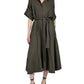 A woman wears the Proenza Schouler Scottie Dress in olive green Eco Stretch Linen Viscose with short sleeves and a self-tie waist belt, paired with black lace-up shoes, standing against a plain white background.