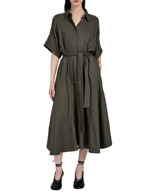A woman wears the Proenza Schouler Scottie Dress in olive green Eco Stretch Linen Viscose with short sleeves and a self-tie waist belt, paired with black lace-up shoes, standing against a plain white background.