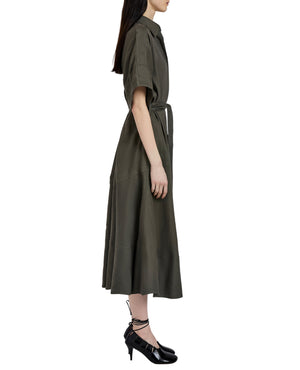 A woman in profile wears the Proenza Schouler Scottie Dress, a dark green eco stretch linen piece with short sleeves and a self-tie waist belt, paired with black lace-up shoes.