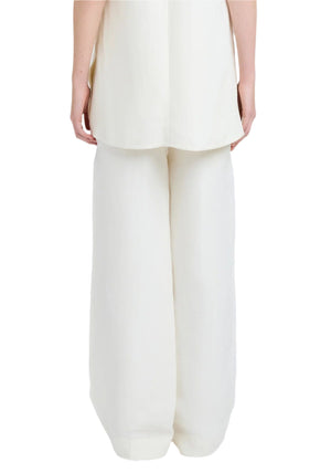 Someone shown from the back wears the Proenza Schouler Maggi Pant—loose-fitting, white slouchy trousers with side slip pockets—paired with a matching white top and their arms relaxed at their sides.