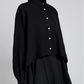 A person wears the Proenza Schouler Zad Classic Twill Top—a black collared shirt with tailored detailing and white buttons—over a black turtleneck and skirt, shown waist up against a plain backdrop.
