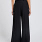 Person seen from the back wears the Proenza Schouler Patricia Classic Twill Pant, featuring a high waist, wide leg, tailored silhouette, and rear welt pockets, set against a plain light background.
