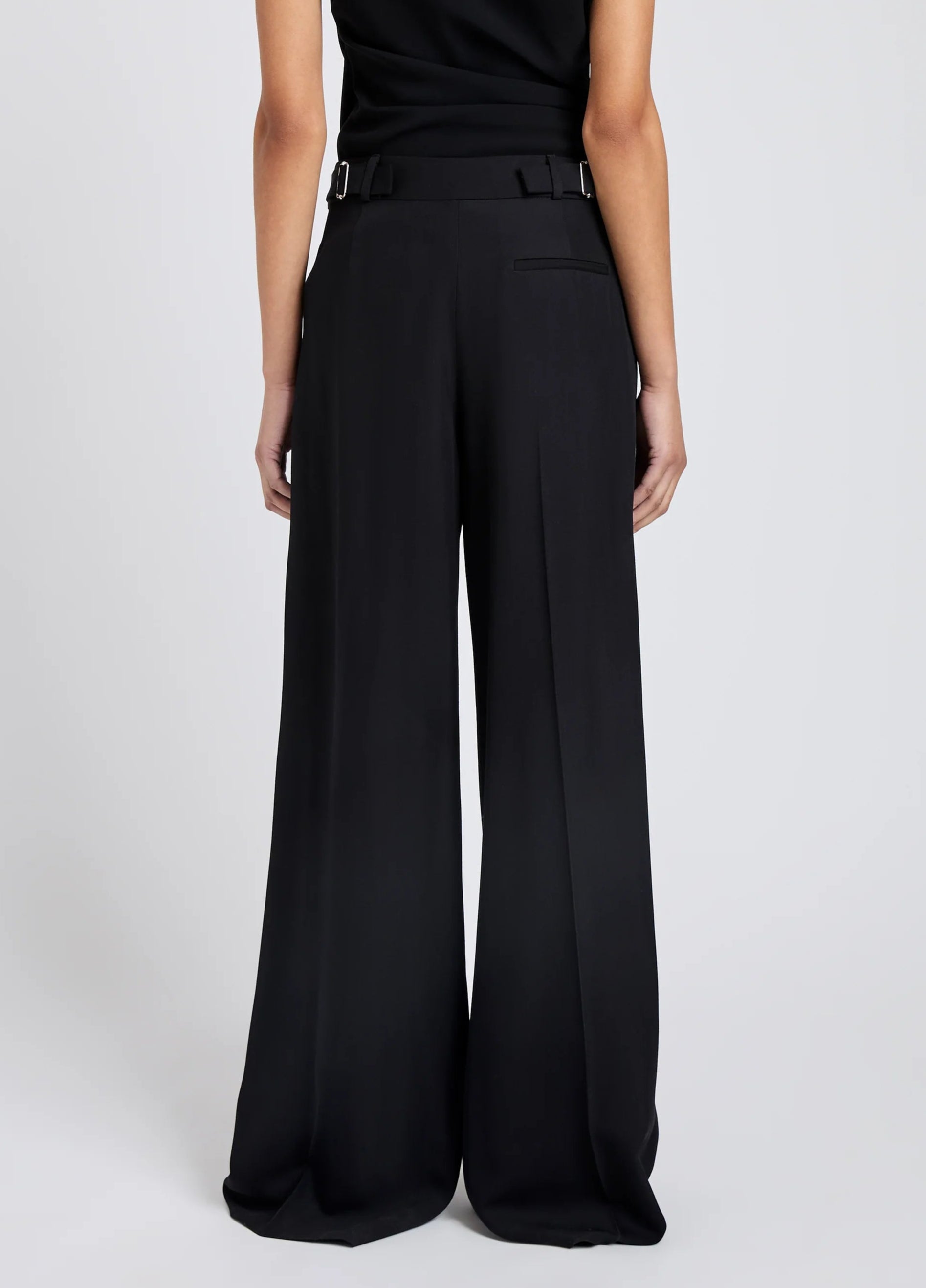Person seen from the back wears the Proenza Schouler Patricia Classic Twill Pant, featuring a high waist, wide leg, tailored silhouette, and rear welt pockets, set against a plain light background.