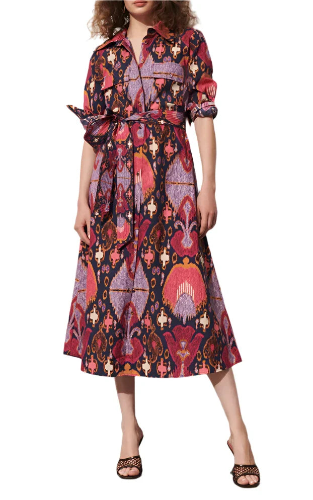 Wearing the Figue Bassa Dress, a vibrant patterned A-line midi dress with a chic collar and button closure, she elegantly ties the waist and enjoys the convenience of side pockets. She completes the look flawlessly with open-toe sandals.