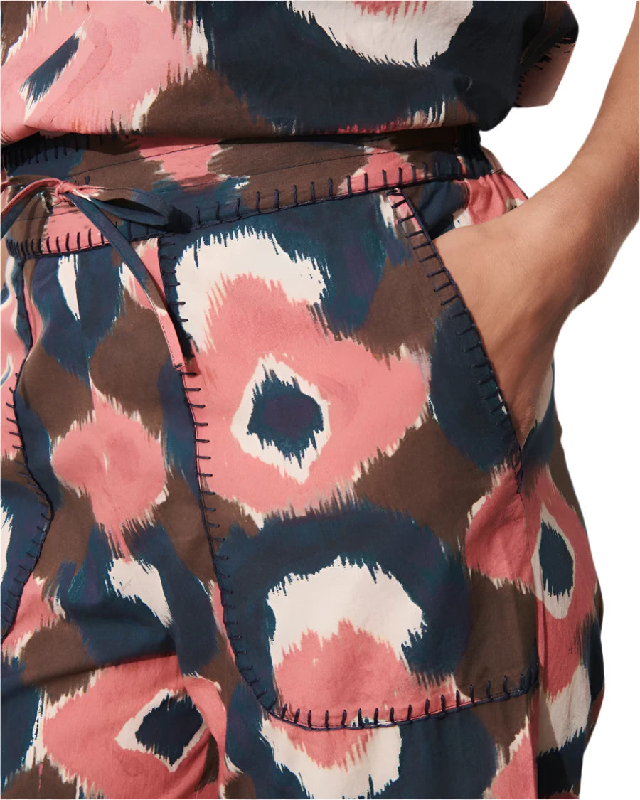 Close-up of a person wearing the Figue Jolie Pant, a colorful garment by Figue featuring an abstract pattern in pink, brown, and blue with front pockets, showing a hand nestled comfortably inside.