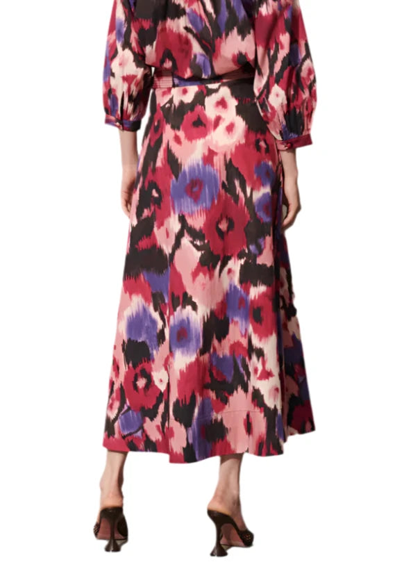 The image shows a person dressed in the Figue Isla Skirt, featuring vibrant floral patterns and a circle cut design with long sleeves, complemented by black high heels from the back view.