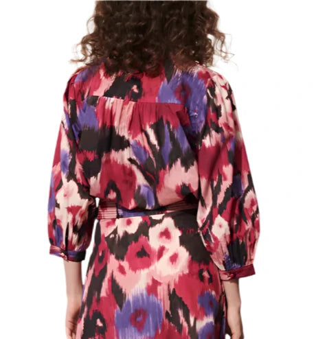 A person with curly hair is shown from the back, wearing a vibrant patterned Figue Danilia Top featuring bracelet-length sleeves.