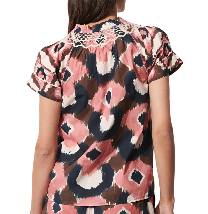 Someone is wearing the Figue Rosie Top, a short-sleeve blouse featuring a smocked neckline and an abstract pattern in pink, brown, and navy, highlighted with intricate crochet detail on the back.