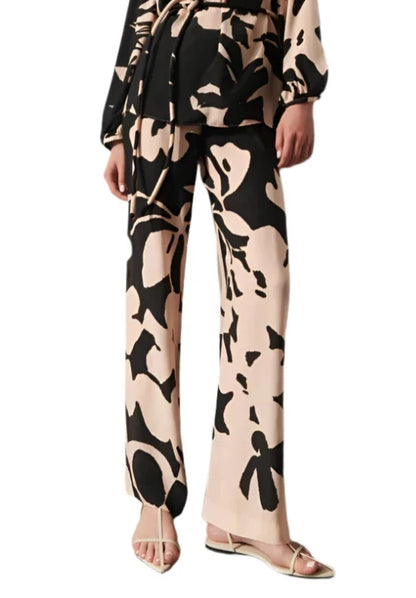 A person is wearing a black and beige patterned outfit with a straight silhouette, featuring long sleeves and Figue's Devon Pants, which have an elastic waistband and a wide-leg design. The ensemble is perfectly paired with beige open-toe sandals.