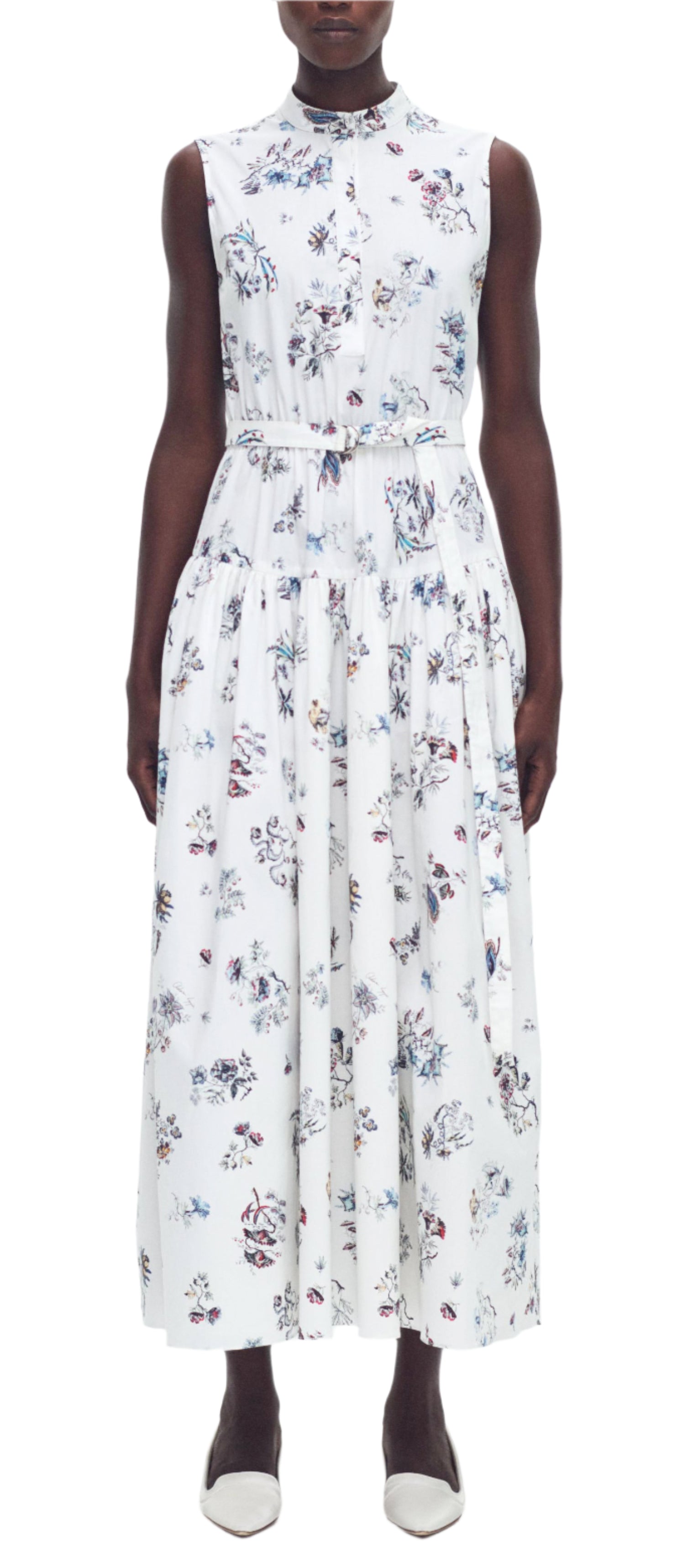 The individual is wearing the elegant Adam Lippes Arden Dress, made from Italian cotton poplin. It showcases a sleeveless, ankle-length floral design with a chic structured band collar, ideally paired with white flat shoes.