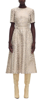 A person in an Eloise Dress Leopard Jacquard by Adam Lippes and beige knee-high boots stands confidently against a plain white backdrop.