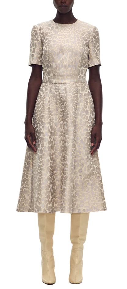 A person in an Eloise Dress Leopard Jacquard by Adam Lippes and beige knee-high boots stands confidently against a plain white backdrop.
