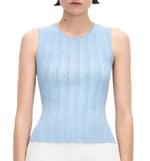 A woman wears the Adam Lippes Brynn Top Compact Jacquard, a sleeveless light blue ribbed knit with a fitted bodice and round neckline, paired with white bottoms and shown from the waist up.
