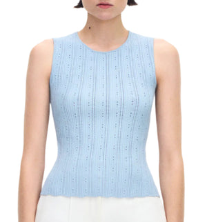 A woman wears the Adam Lippes Brynn Top Compact Jacquard, a sleeveless light blue ribbed knit with a fitted bodice and round neckline, paired with white bottoms and shown from the waist up.